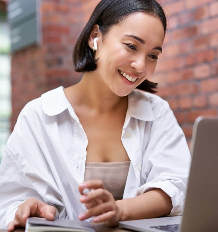 young-smiling-asian-woman-with-wireless-earphones-sitting-in-coworking-office-space-with-laptop.jpg
